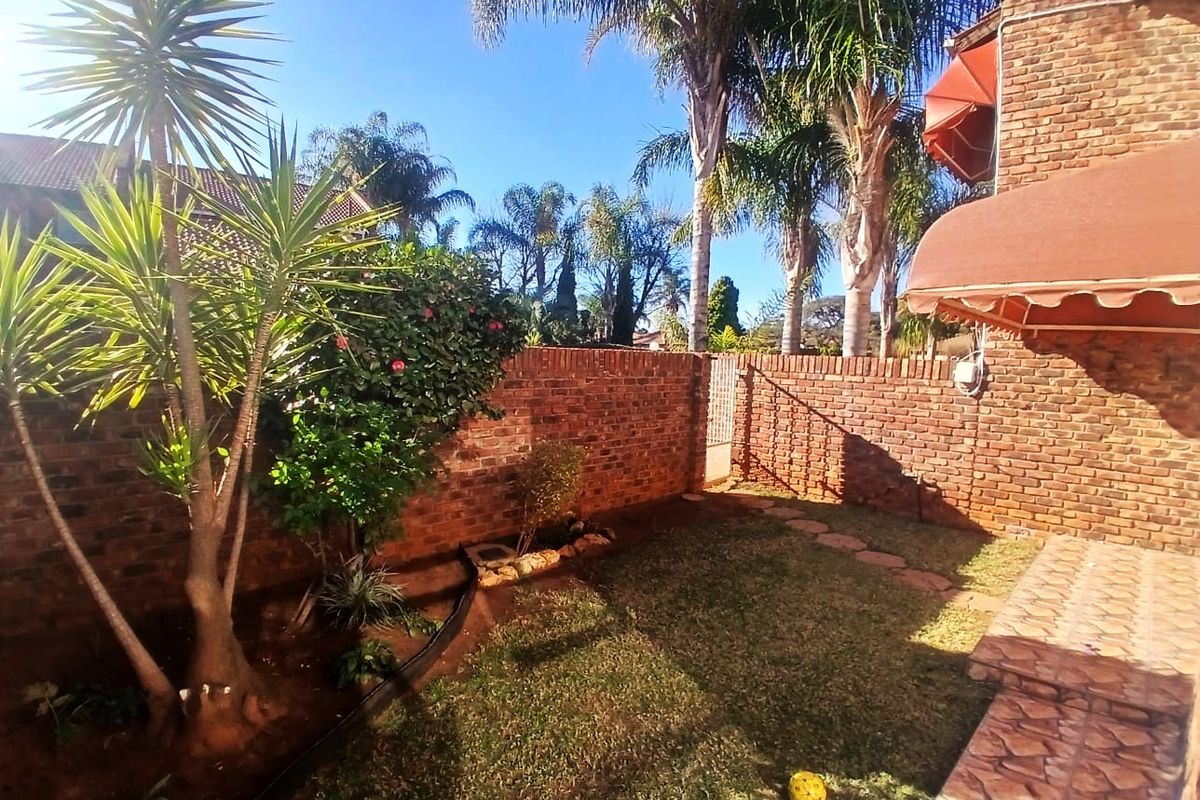 A private rear garden featuring a brick boundary wall, a paved patio area with a retractable awning, and established landscaping.