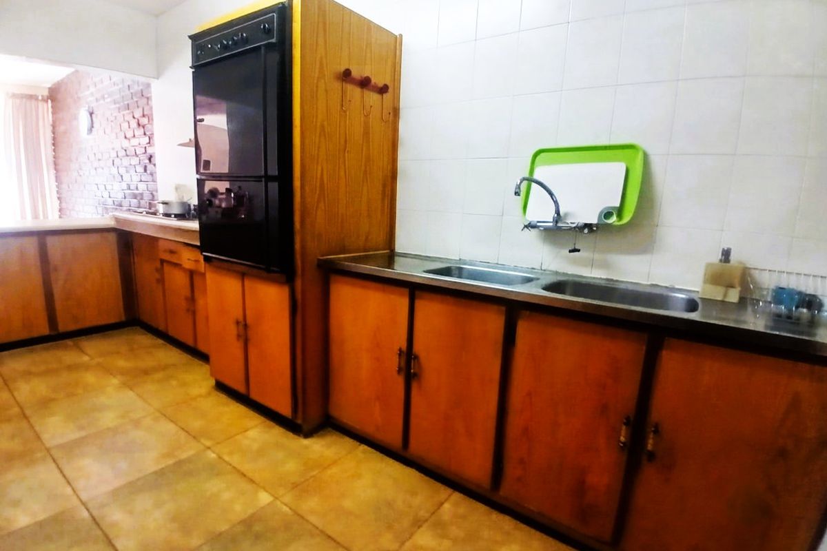 A dated kitchen featuring wood-finish cabinetry, a built-in oven, and a double stainless steel sink with tiled splashbacks.