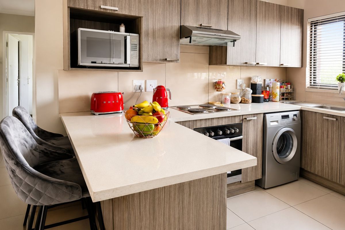 Modern kitchen featuring wood-grain cabinetry, quartz countertops, built-in appliances including an oven, hob, extractor, and integrated washing machine with a breakfast bar.