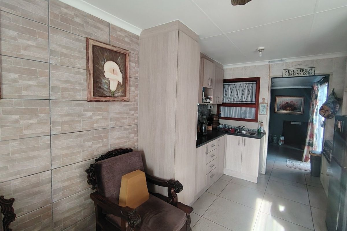 A functional kitchen area featuring light-toned built-in cabinetry, dark countertops, a stainless steel sink, and tiled flooring with a tiled feature wall.