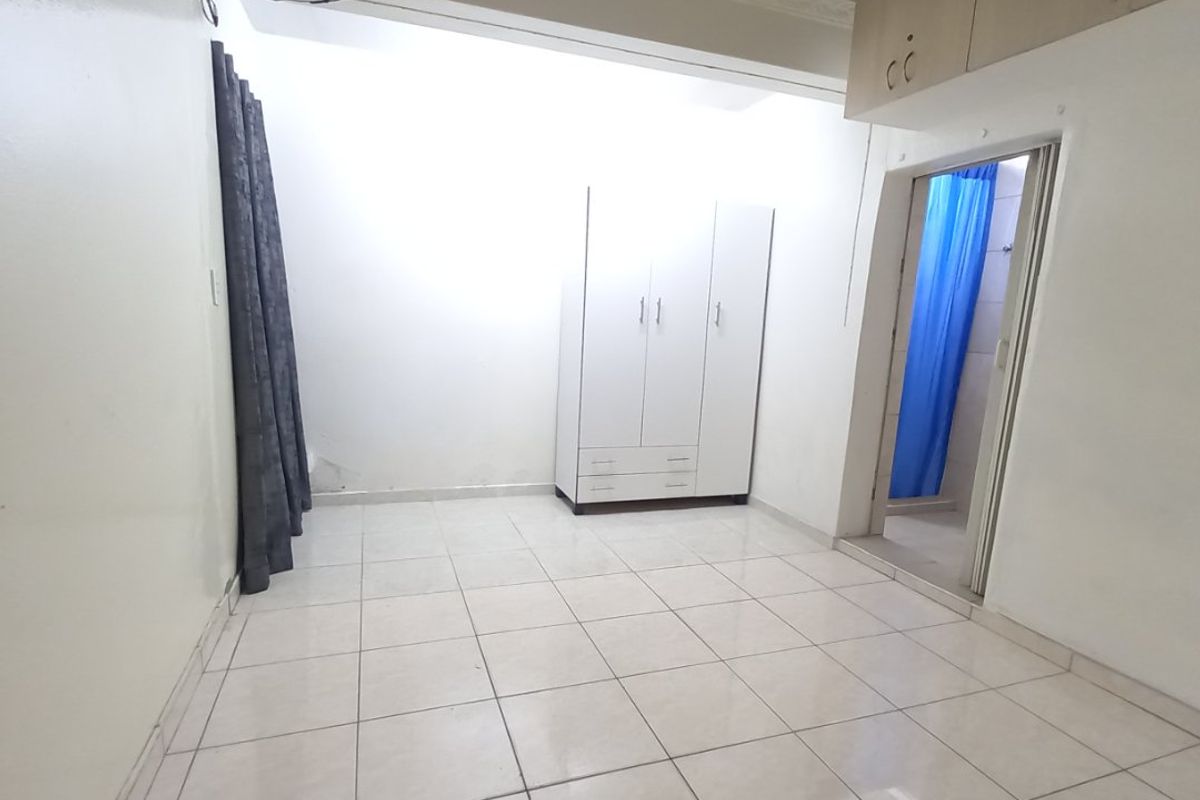 A vacant bedroom featuring tiled flooring, built-in cupboards, and overhead storage, with an adjacent doorway leading to a bathroom area.