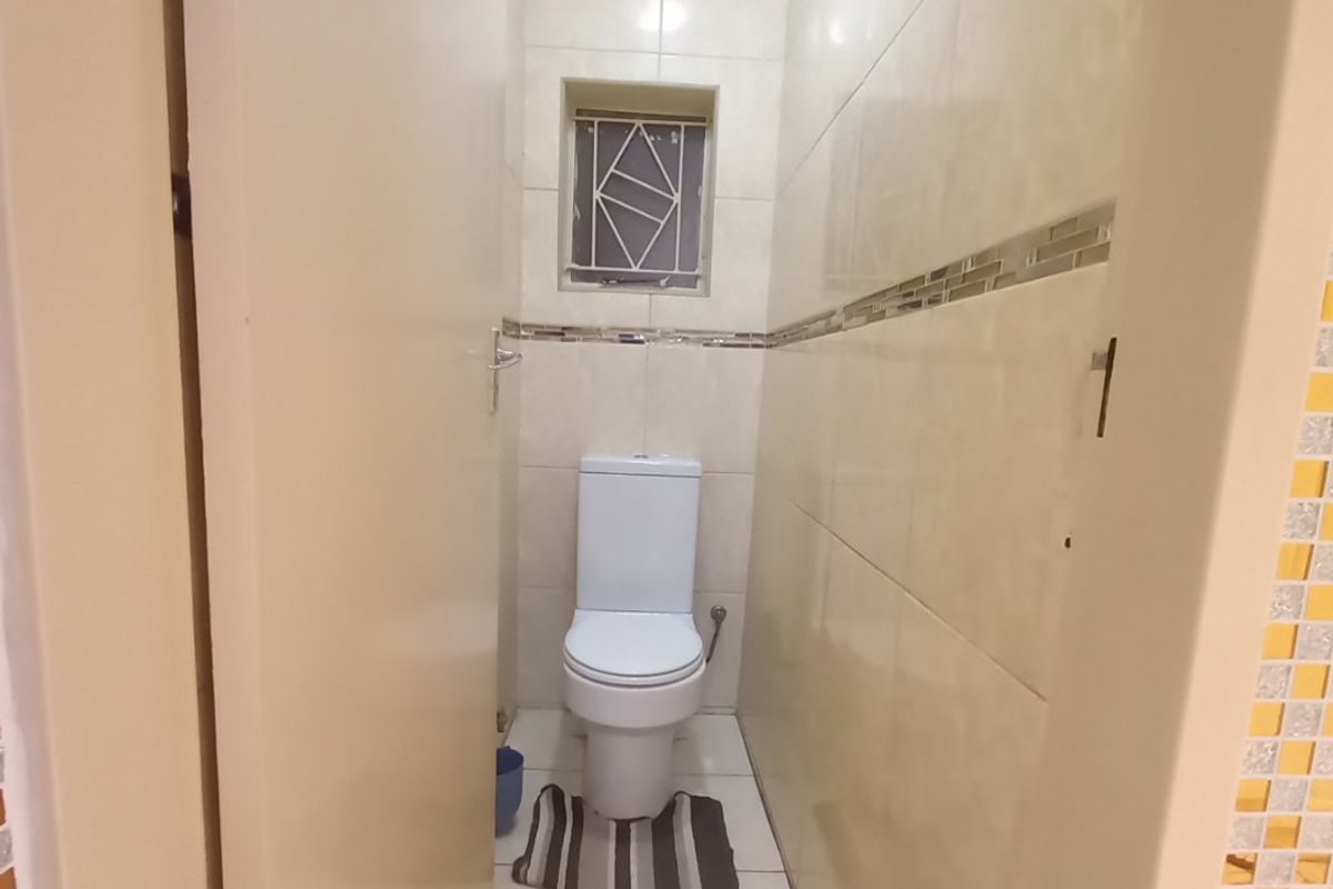 A compact, tiled guest toilet featuring neutral wall tiles with a decorative border and a secure window.
