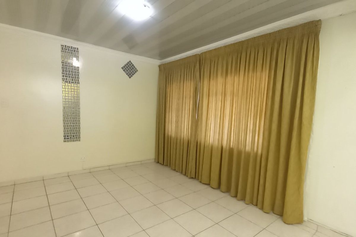 An empty living room featuring tiled flooring, a decorative wall mirror, and ceiling paneling, offering a blank canvas for personalization.