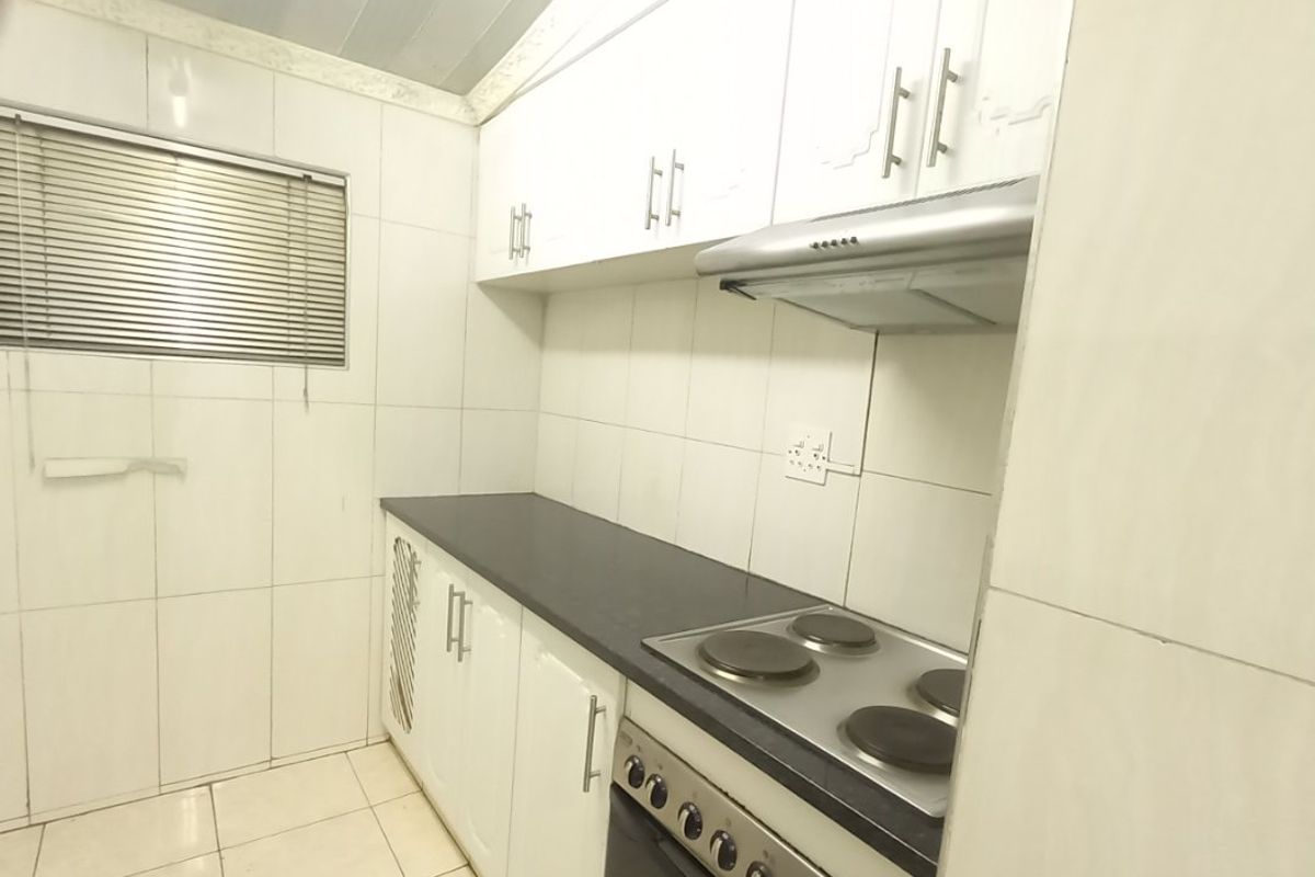 A functional kitchen featuring white built-in cabinetry, a dark countertop, an integrated electric stove with oven, and fully tiled wall and floor surfaces.