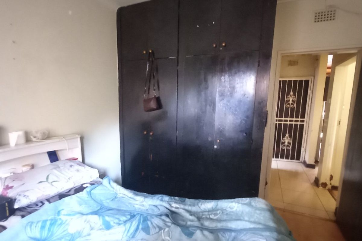 A bedroom featuring a large built-in wardrobe with dark finish, showing signs of wear and requiring cosmetic updates.