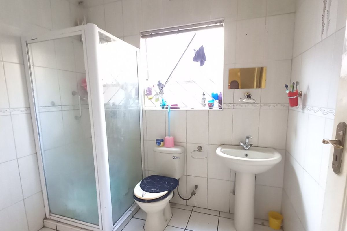 A functional bathroom featuring a shower enclosure, pedestal basin, and toilet, finished with white ceramic wall and floor tiles.