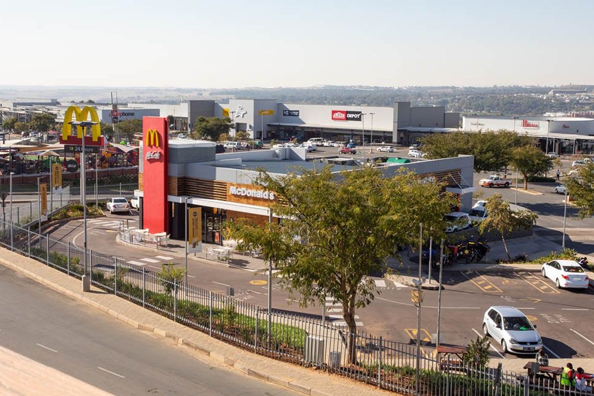 Aerial view of a commercial fast-food restaurant property featuring a drive-thru lane, paved parking area, and perimeter fencing within a retail complex.