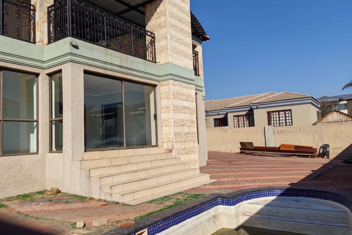 Rear exterior view featuring a swimming pool, paved courtyard, and a multi-level structure with a balcony and sliding glass door access.