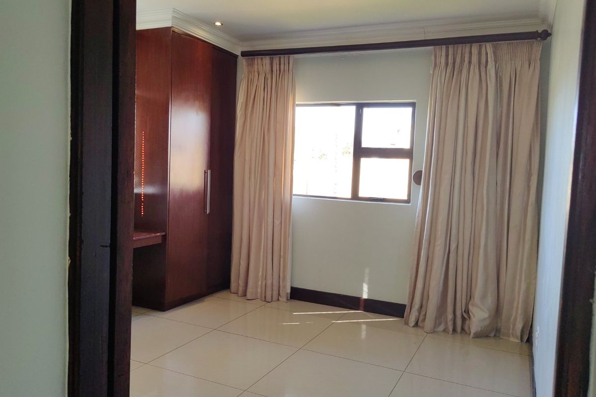 A bright, empty bedroom featuring tiled flooring, built-in wooden cupboards, and recessed ceiling lighting.