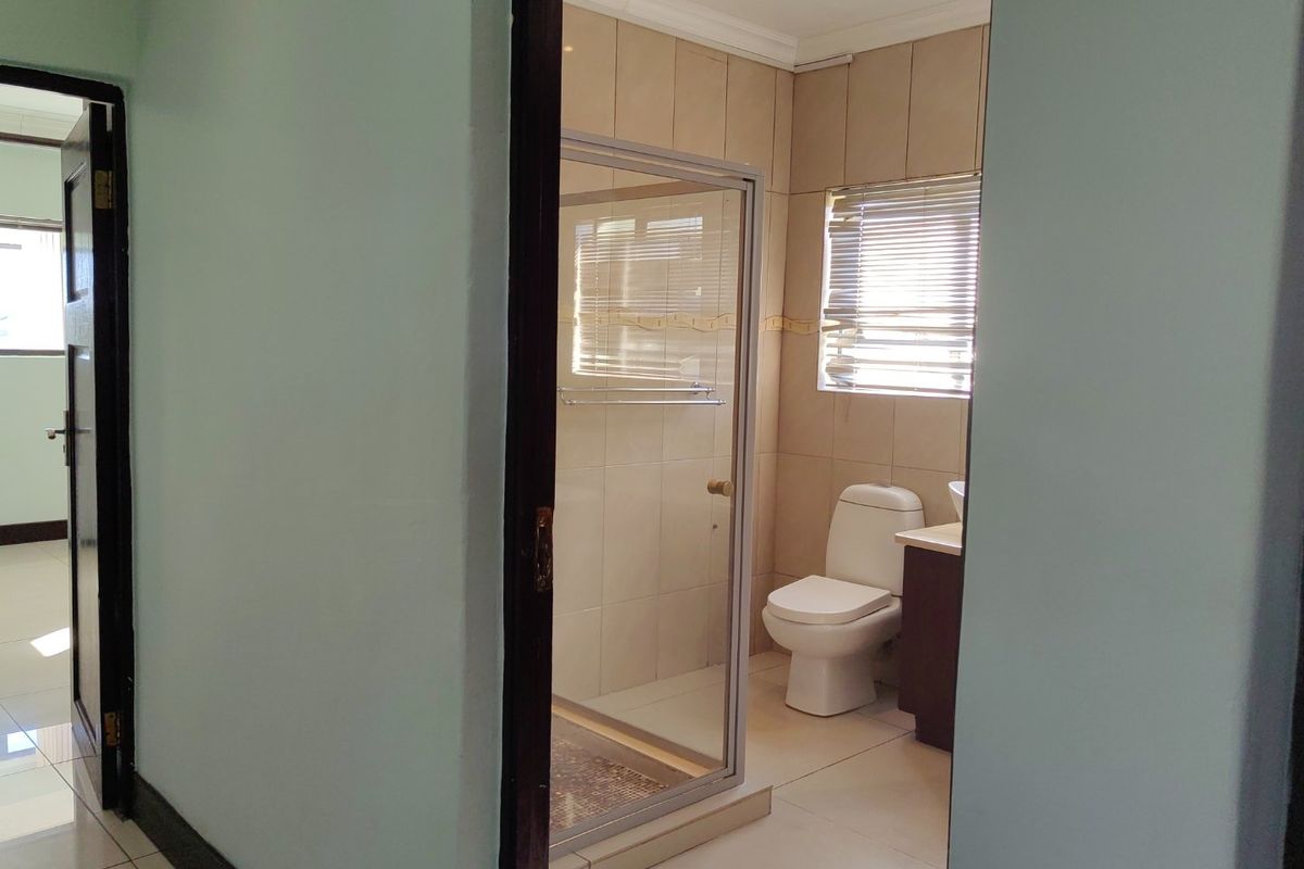 A functional bathroom featuring a glass-enclosed shower, a toilet, and a vanity basin with neutral wall and floor tiling.