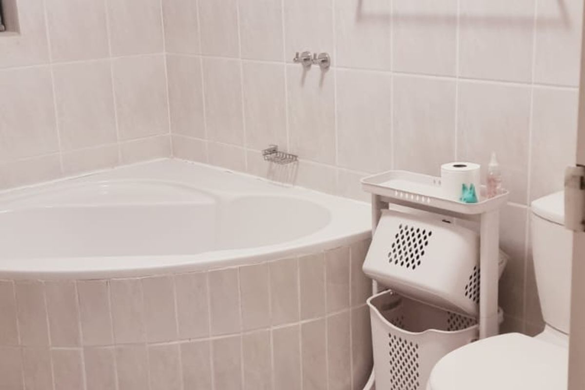 A functional bathroom featuring a corner bathtub, tiled walls and flooring, and a standard toilet suite.