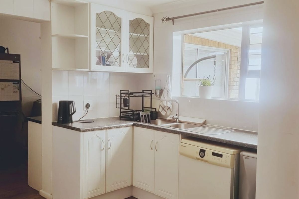 A functional kitchen featuring white cabinetry, leaded glass display cupboards, laminate countertops, and a stainless steel sink with a view to the exterior.