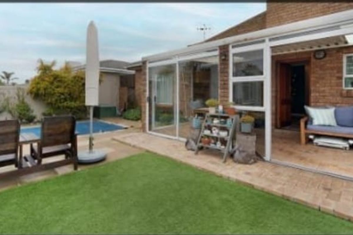 A covered patio area with sliding glass doors, brick exterior, and direct access to a backyard swimming pool and lawn.