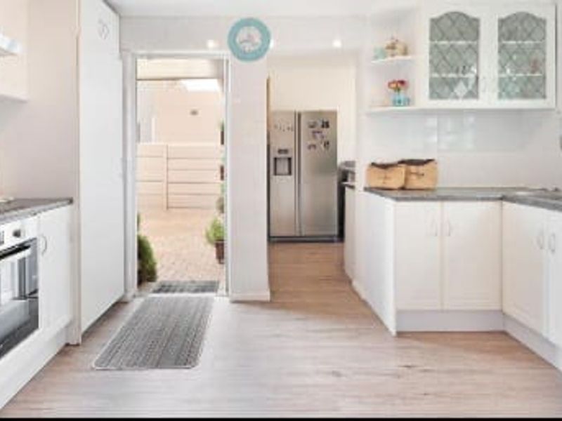 A functional kitchen featuring white cabinetry, stone countertops, built-in oven, and extractor fan, with direct access to an outdoor area.