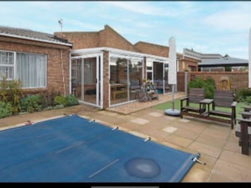 Rear exterior view featuring a paved patio area, swimming pool with cover, and an enclosed sunroom attached to the brick house structure.