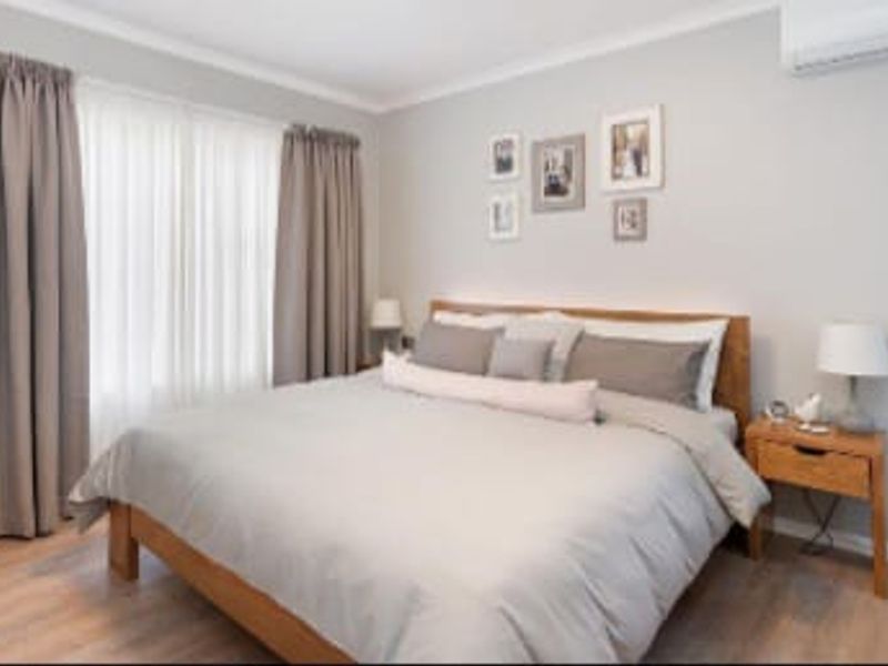A well-maintained bedroom featuring light-toned laminate flooring, neutral wall finishes, and a wall-mounted split-system air conditioning unit.