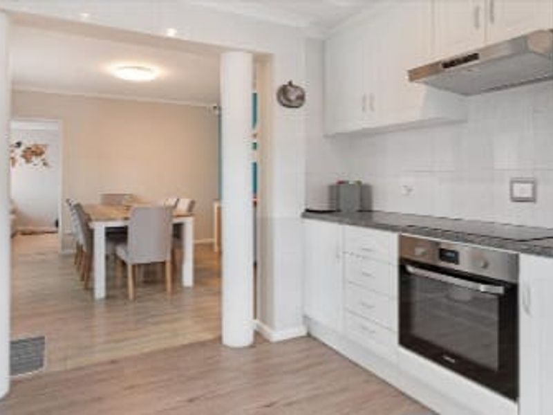 Open plan kitchen and dining area featuring white cabinetry, modern built-in appliances, and light wood-look flooring, creating a bright and functional living space.