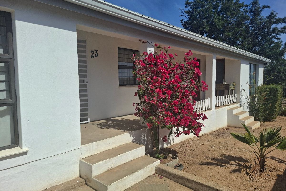 Front elevation of the house featuring a covered veranda, concrete steps, and security gate access.