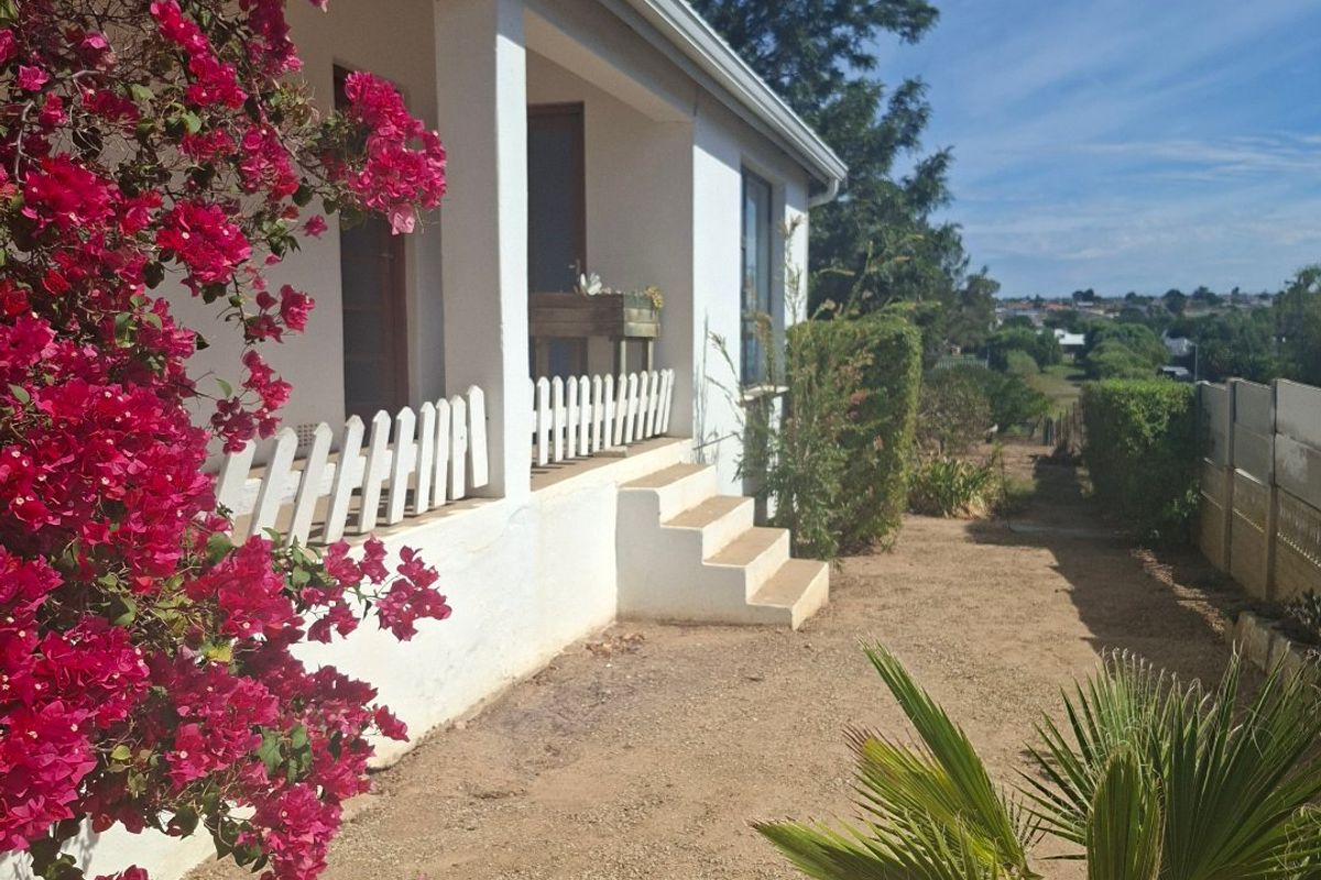 A rear view of the house featuring a covered patio, concrete steps, and a picket fence overlooking the garden area.