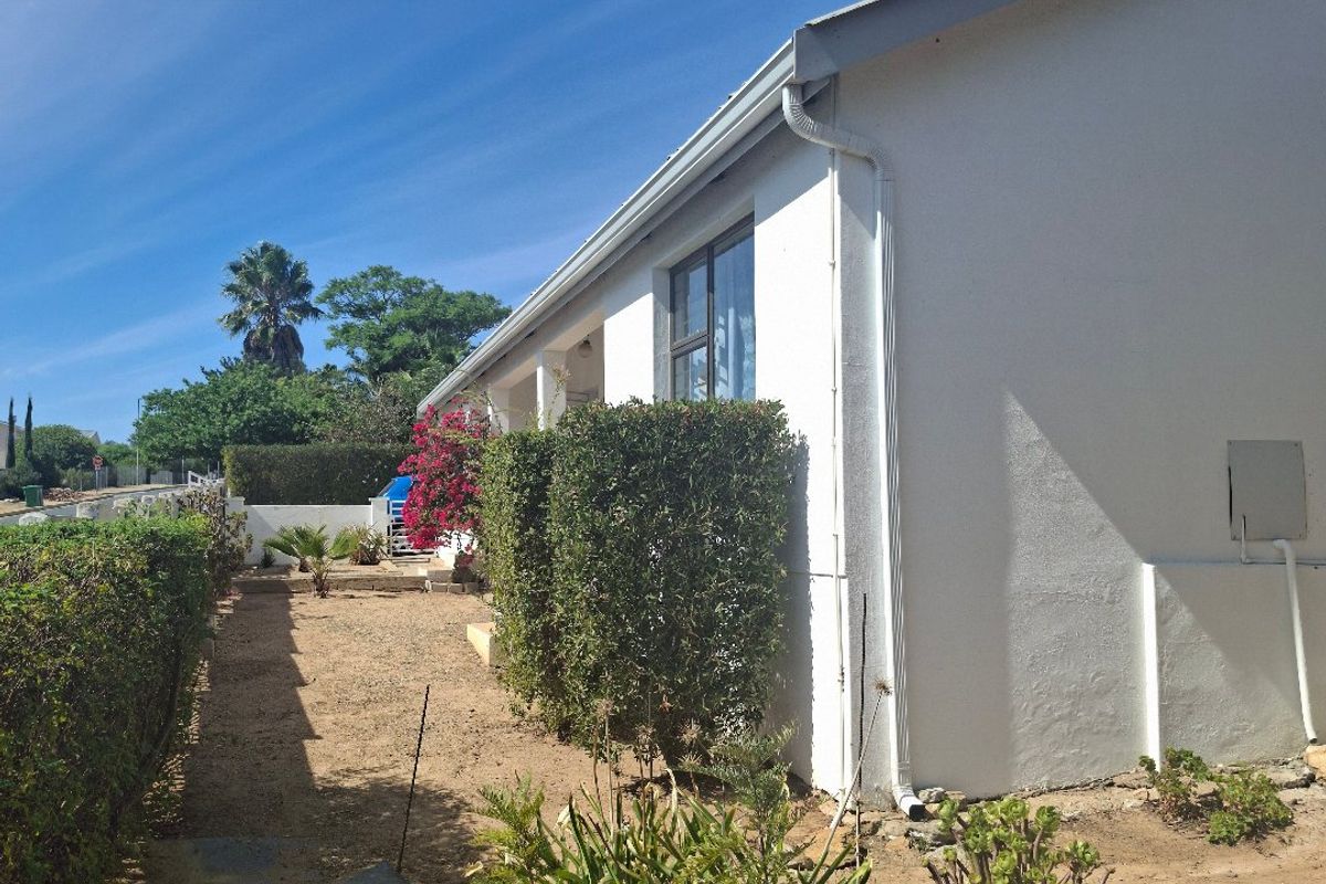 A side view of the property showing the exterior wall, guttering system, and a narrow garden path leading toward the rear yard.