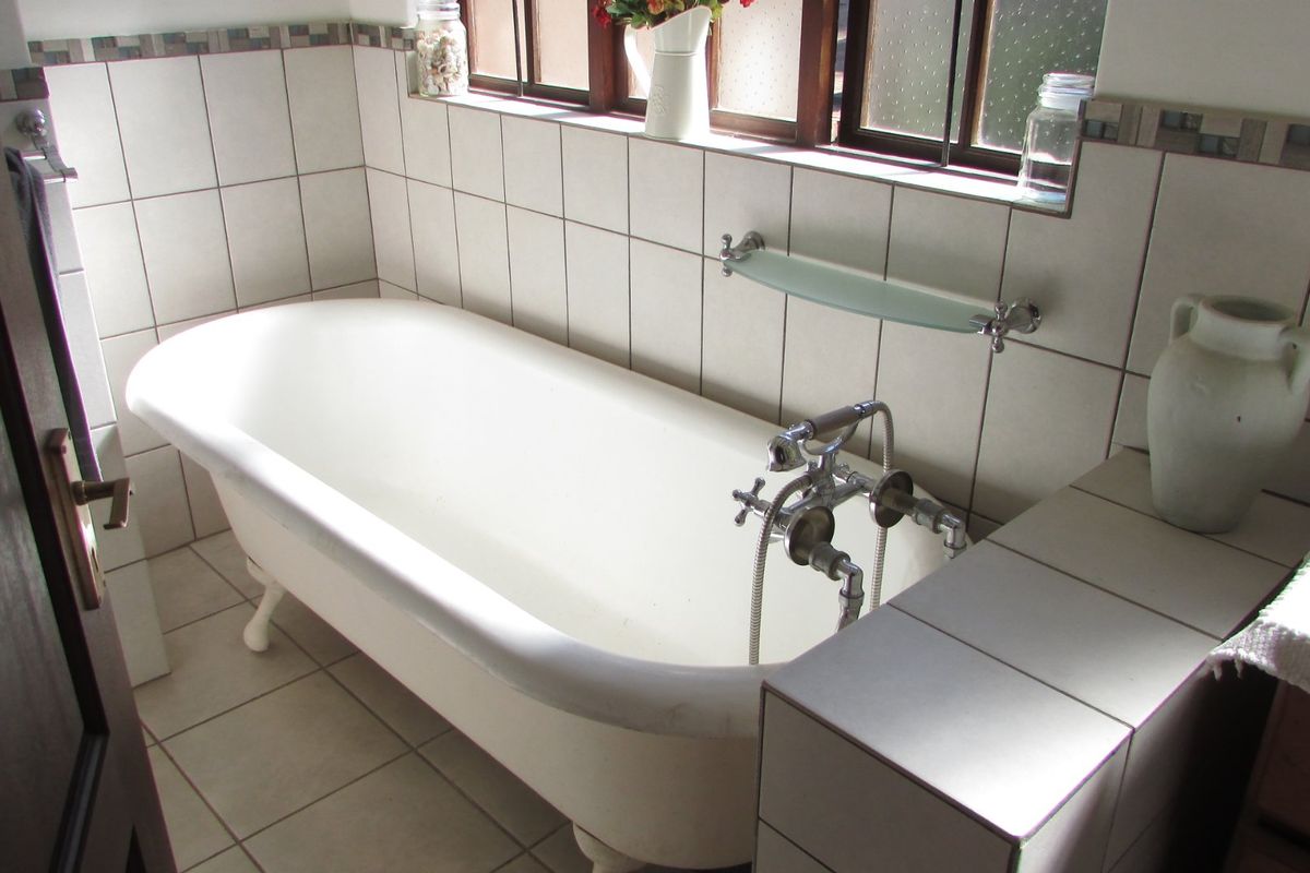 A bathroom featuring a classic clawfoot bathtub, tiled walls and flooring, and a vintage-style faucet set beneath a timber-framed window.