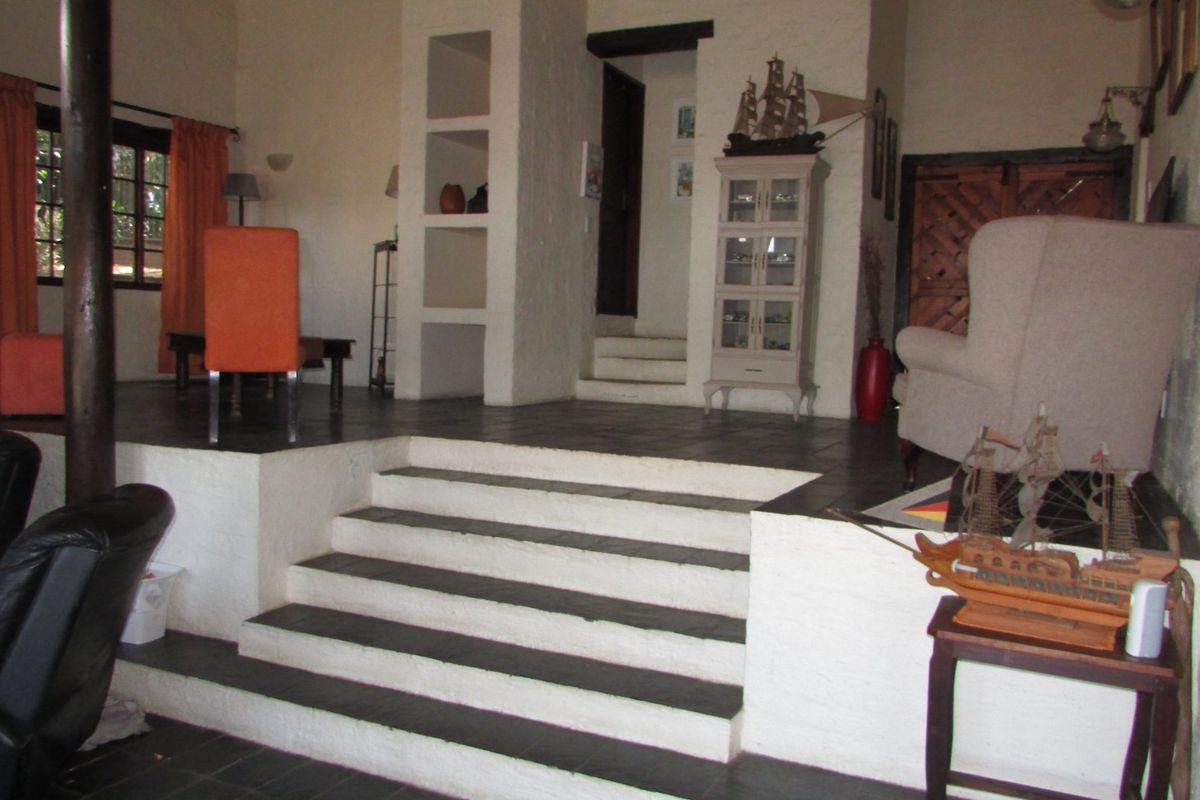 Spacious sunken living room featuring textured white walls, stone tile flooring, and built-in display shelving with a central staircase.