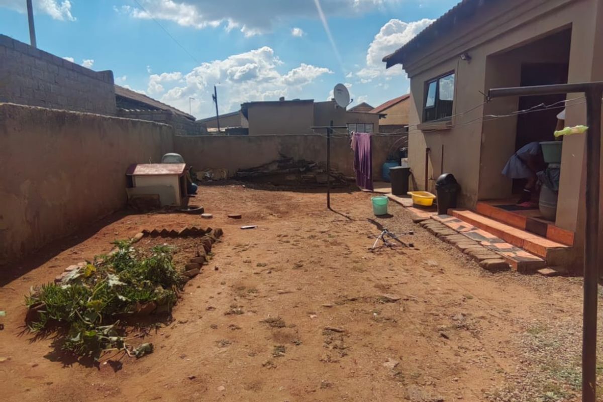 Rear exterior view of the property featuring a large unlandscaped yard, perimeter boundary walls, and tiled entrance steps leading into the home.