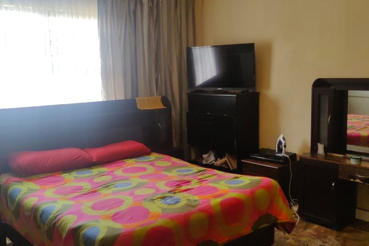 A bedroom featuring tiled flooring and curtain rails, currently showing signs of wear and dated finishes.