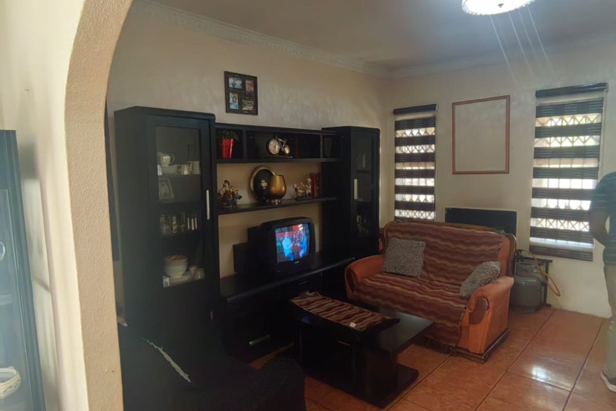 A living room featuring an arched entryway, ceramic floor tiles, and window roller blinds, providing a functional and traditional living space.