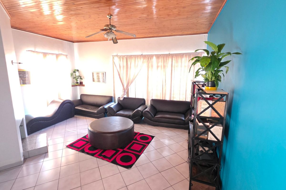 A spacious living room featuring a timber-paneled ceiling, ceiling fan, and neutral tiled flooring, offering a versatile layout for comfortable family living.