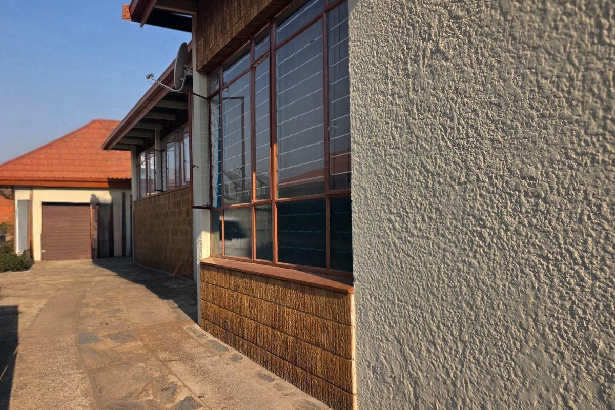A view of the rear exterior showing a paved walkway, textured plaster walls, face brick accents, and steel-framed windows.