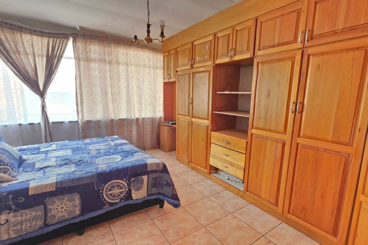 A bedroom featuring extensive built-in wooden cabinetry, tiled flooring, and large windows allowing natural light.