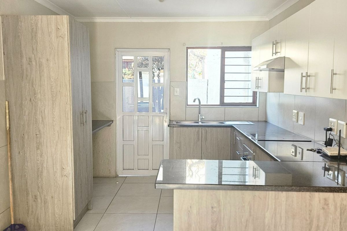 A functional kitchen featuring modern wood-look cabinetry, granite countertops, a stainless steel sink, and direct access to the exterior via a security door.