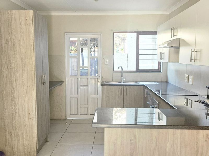 A functional kitchen featuring modern wood-look cabinetry, granite countertops, a stainless steel sink, and direct access to the exterior via a security door.