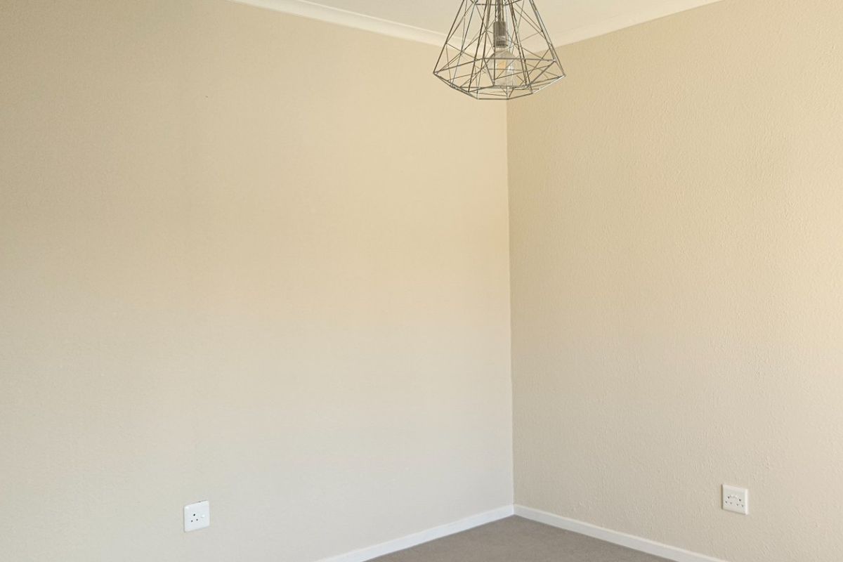 A clean, empty bedroom featuring neutral walls, carpeted flooring, and a modern geometric pendant light fixture.