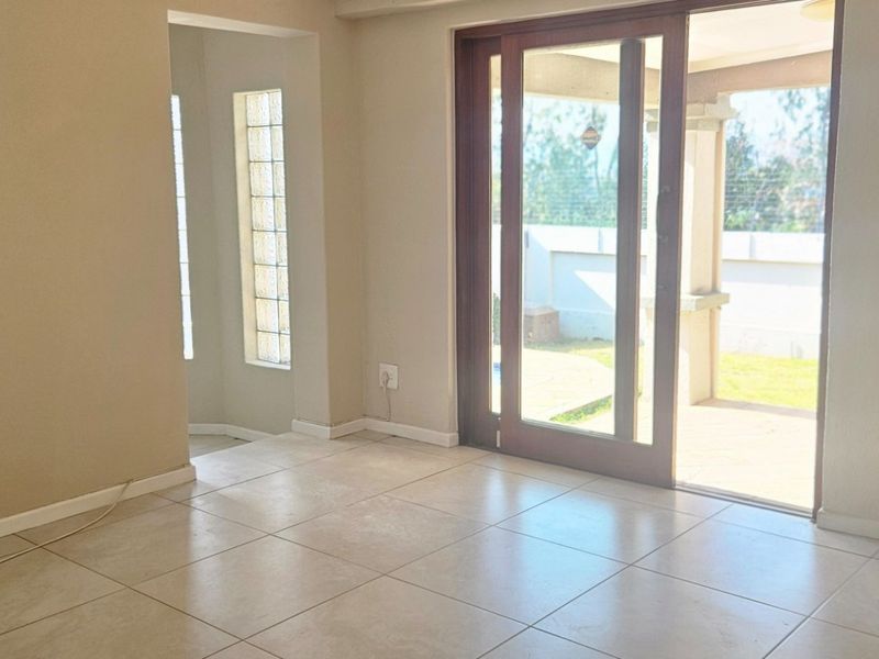 An empty living room featuring neutral ceramic floor tiles, a glass block window, and large sliding doors providing access to the outdoor patio area.
