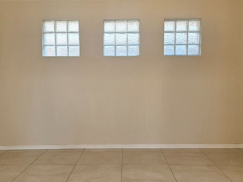 An empty living area featuring neutral wall tones, ceramic floor tiles, and three decorative glass block windows providing natural light.