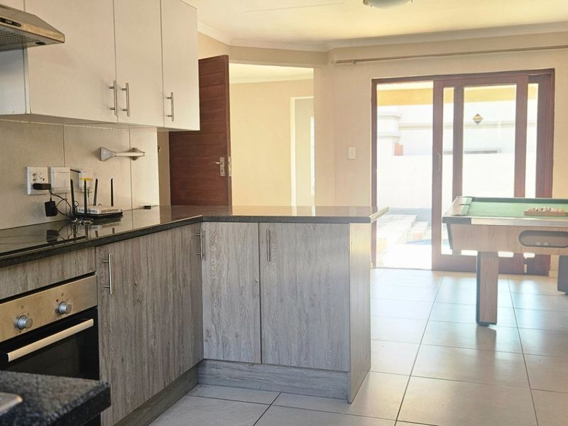 Open-plan kitchen featuring modern cabinetry, granite countertops, and integrated appliances, flowing into a living area with direct access to the patio through sliding doors.