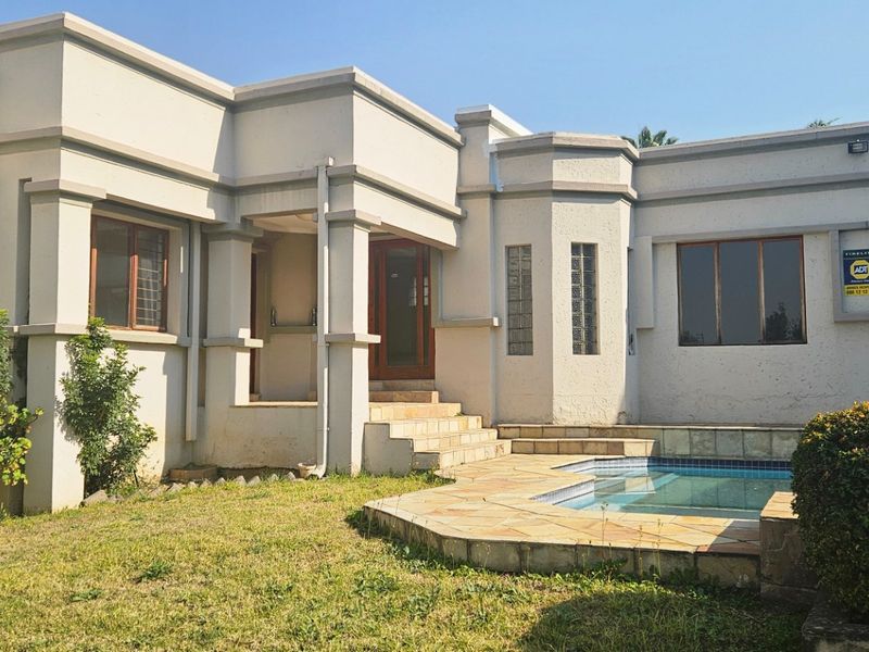Rear exterior view of the townhouse featuring a private swimming pool, stone patio area, and established garden landscaping.