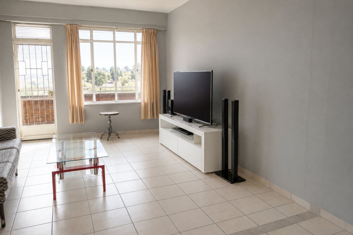 A bright living room featuring neutral tiled flooring, large windows providing natural light, and direct access to an outdoor balcony area.