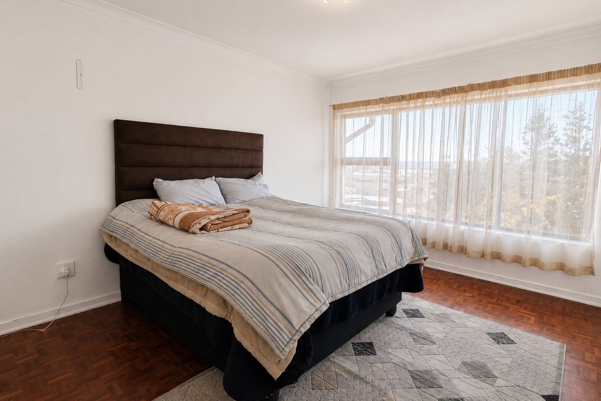 A bedroom featuring classic parquet flooring, a large window with natural light, and neutral wall finishes.