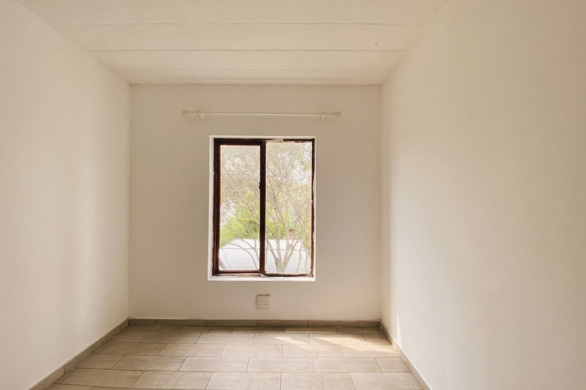 A vacant bedroom featuring neutral tiled flooring, a central window with a curtain rod, and clean white walls, ready for personalization.