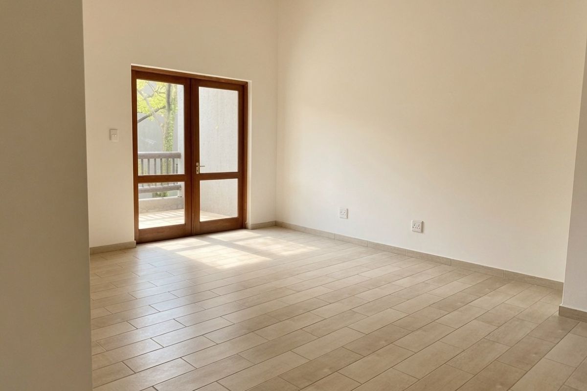 A bright, empty living area featuring neutral tiled flooring and double glass doors providing access to an outdoor space.