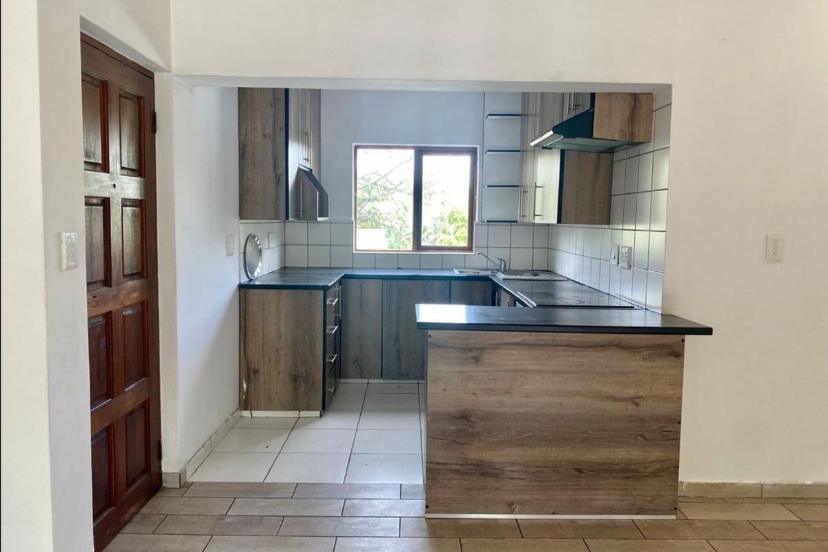 A compact, functional kitchen featuring wood-look cabinetry, dark laminate countertops, a tiled backsplash, and an integrated hob with an extractor fan.