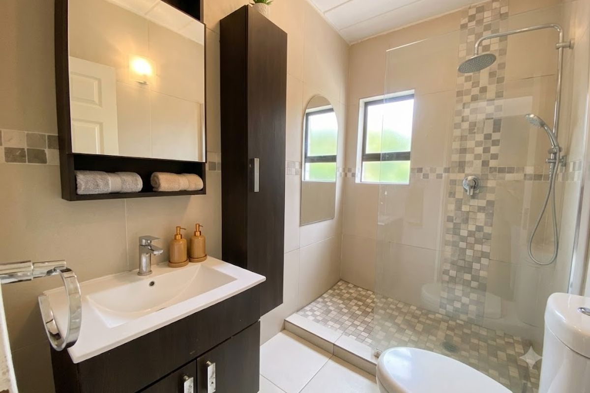 Modern bathroom featuring a walk-in shower with mosaic tile accents, a vanity with storage, and a wall-mounted mirror.