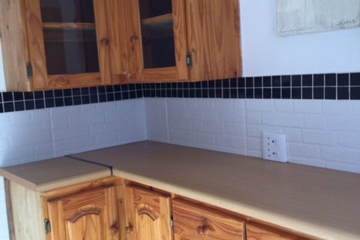 A kitchen corner featuring traditional wooden cabinetry, a laminate countertop, and a decorative black and white tiled backsplash.