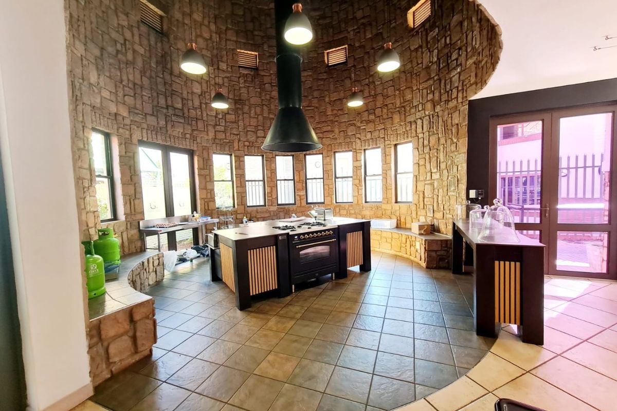 Unique circular kitchen featuring stone-clad walls, a central island with built-in oven and hob, and large windows providing ample natural light.