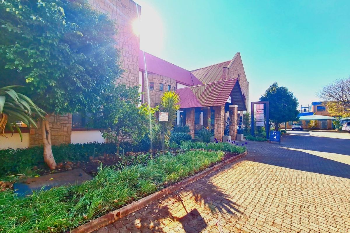 Front elevation of a commercial property featuring stone cladding, a covered entrance, and a paved driveway with established garden beds.