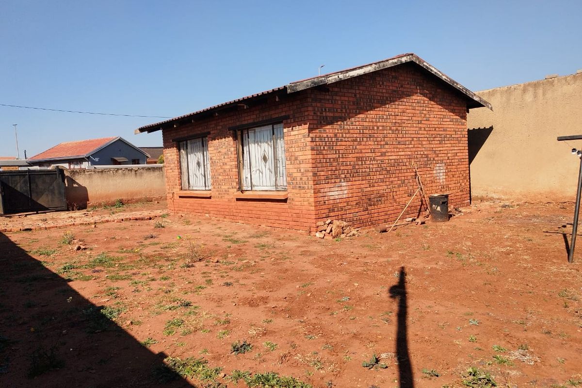 Rear view of a face brick house featuring security bars on windows and a large, unlandscaped yard area enclosed by a perimeter wall.