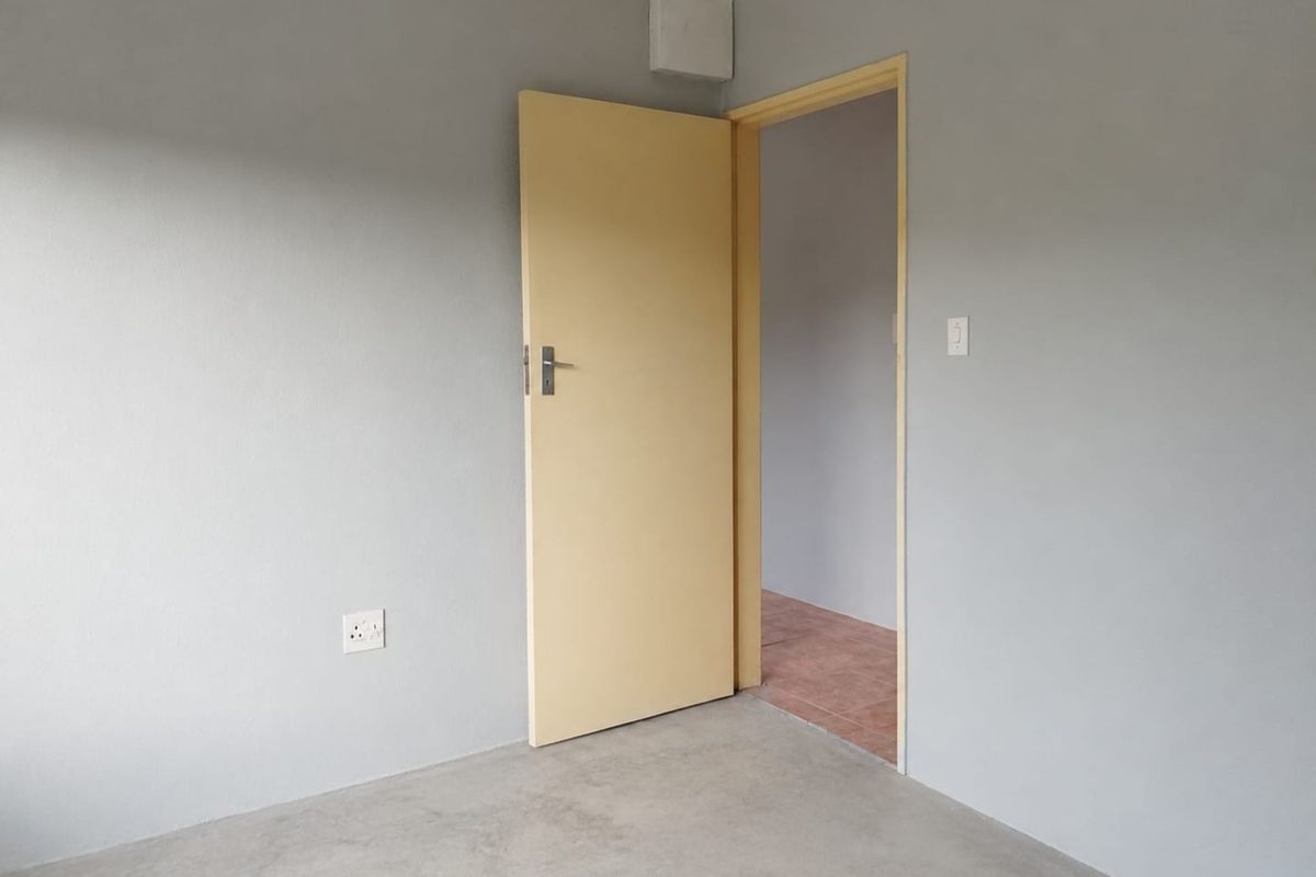 An empty bedroom featuring grey painted walls, concrete flooring, and a simple internal door leading to an adjacent space.